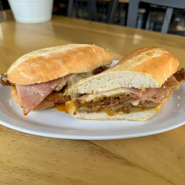 Two Mexican torta sandwiches with ham, cheese, and meat on a white plate.