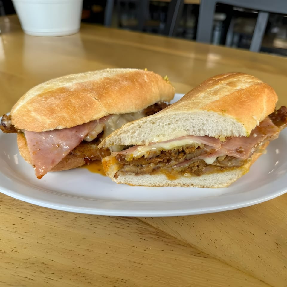 Two Mexican torta sandwiches with ham, cheese, and meat on a white plate.