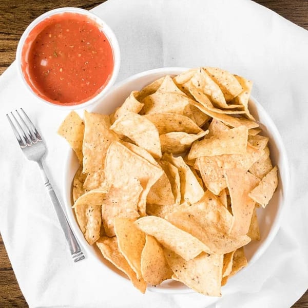 A white bowl of tortilla chips and a small bowl of red salsa on a white napkin.
