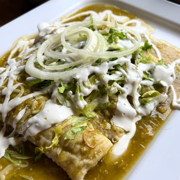 Mexican enchiladas covered in green sauce, sour cream, shredded lettuce, and sliced onions.