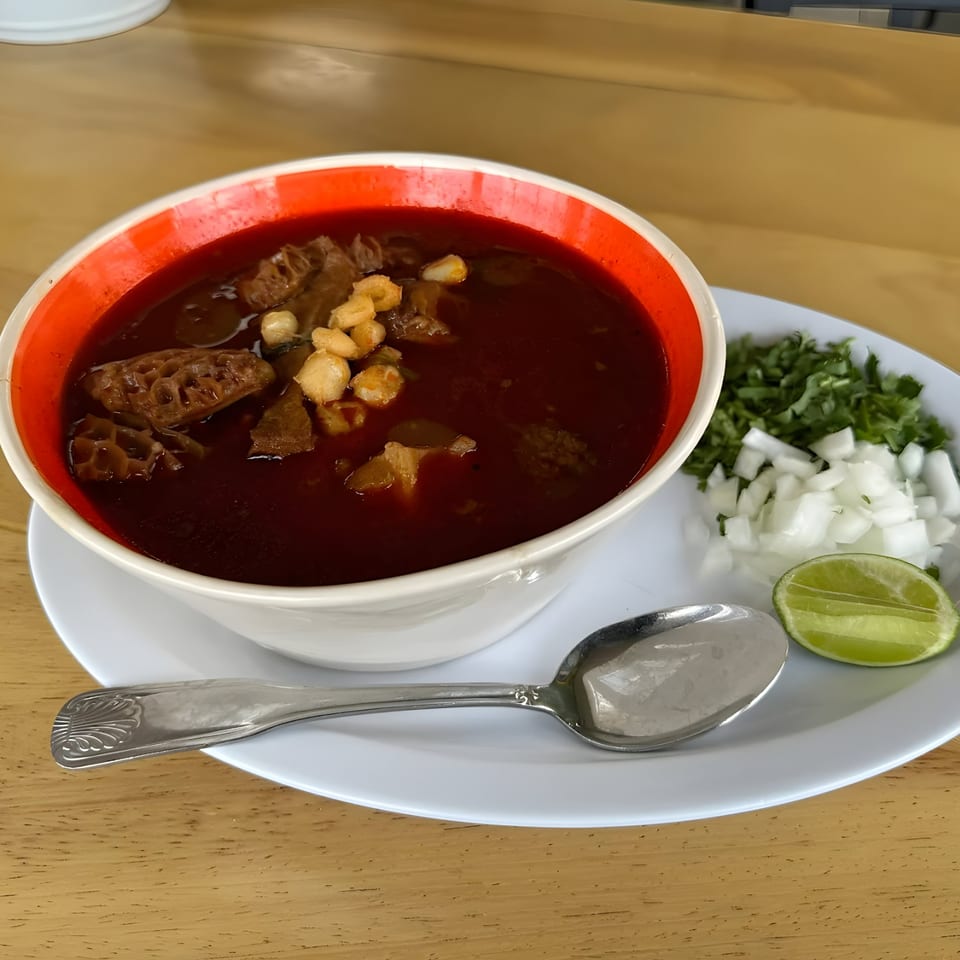 Menudo soup with tripe, hominy, and a side of chopped onions, cilantro, and lime.