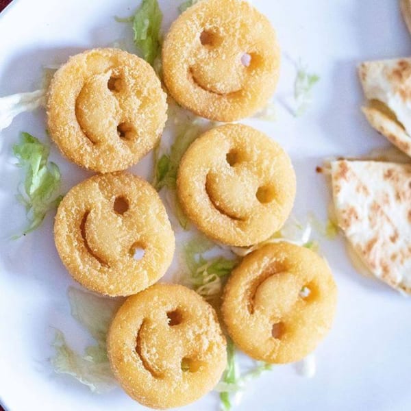 Six golden-brown smiley face fries on a white plate with shredded lettuce and quesadilla wedges.