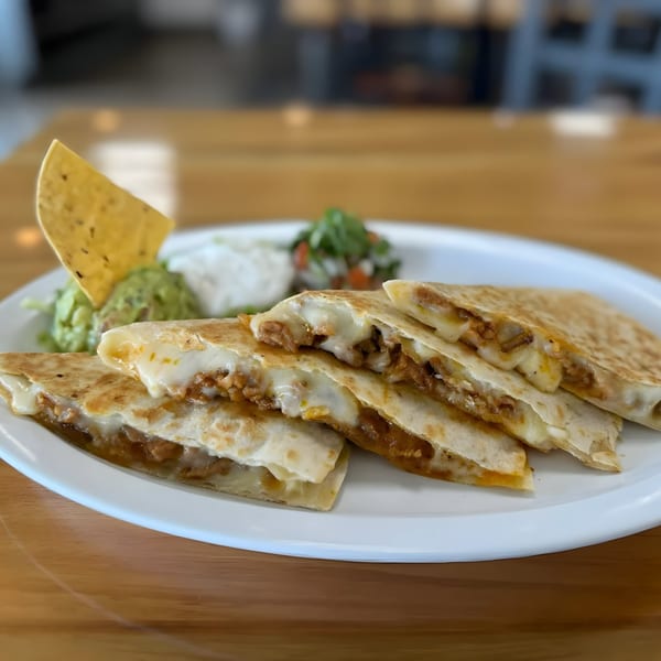 Four cheesy quesadilla slices with guacamole, sour cream, and salsa on a white plate.